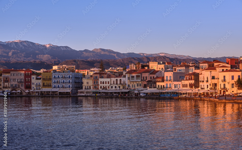 Sunrise at Old Venetian harbour of Chania, Crete, Greece, shop, hotels, cafes and restaurants on its quay in first sunrays. Cretan hills and mountains