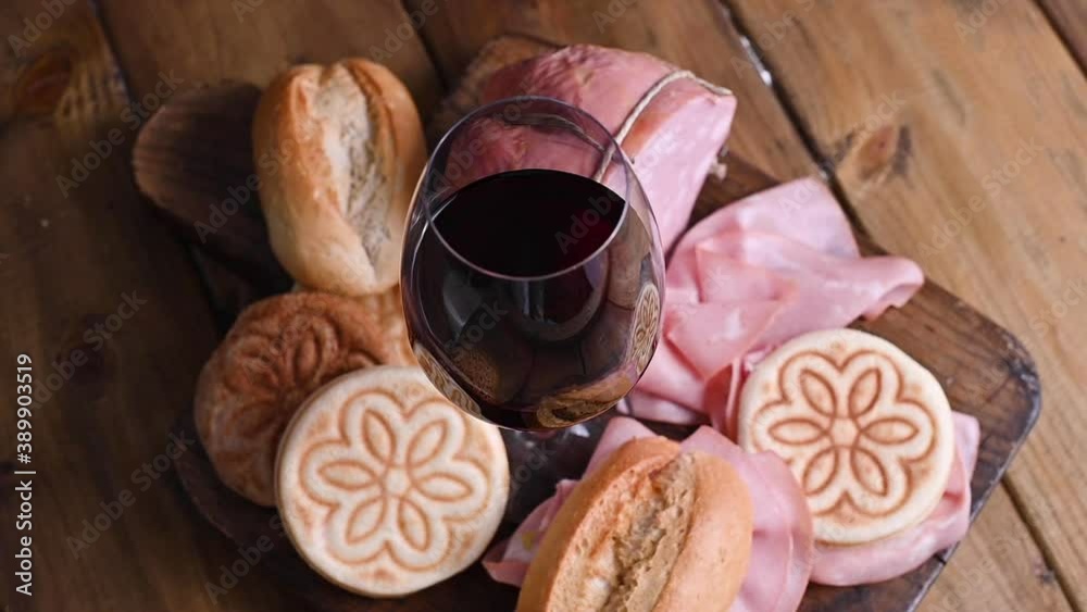 A glass of red wine, mortadela, Tigelle and different breads on a wooden table. A traditional pre-dinner starter in the northern Italian region of Emilia Romagna. footage A glass of red wine, mortadela, Tigelle and different breads on a wooden table. A traditional pre-dinner starter in the northern Italian region of Emilia Romagna. footage