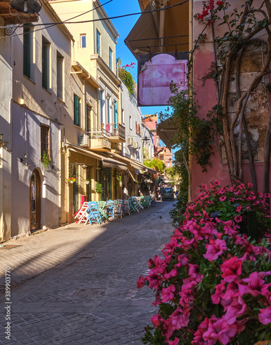 Fototapeta Naklejka Na Ścianę i Meble -  Beautiful view of narrow streets of old town of Chania, Crete, Greece in early morning. Street cafes and restaurants. Selective focus. Pink petunia.