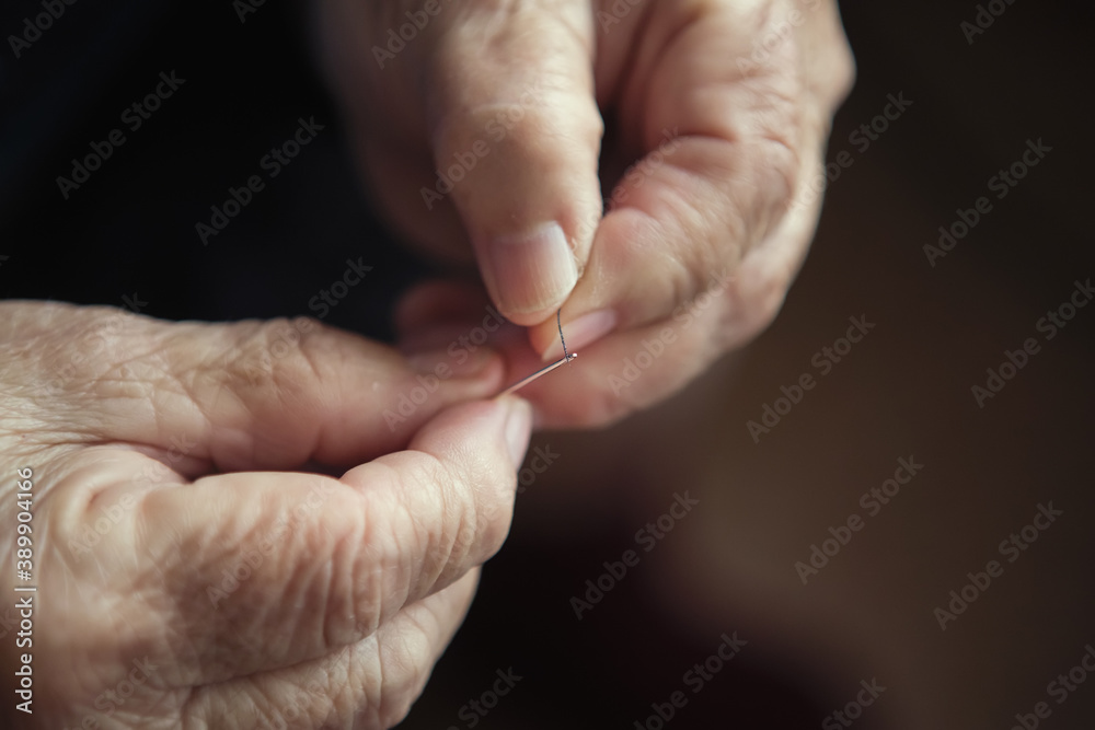 Old woman's hands are threaded in the needle.