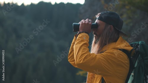 Caucasian hipster man using binoculars birdwatching or looking at natural scenery searching ways traveling with group of friends. Nature concept. Forest environment. Camping.