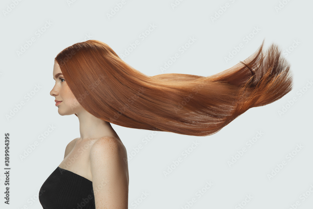 Silk. Beautiful model with long smooth, flying red hair isolated on white  studio background. Young girl with well-kept skin and hair blowing on air.  Concept of salon care, beauty, fashion. Stock Photo |