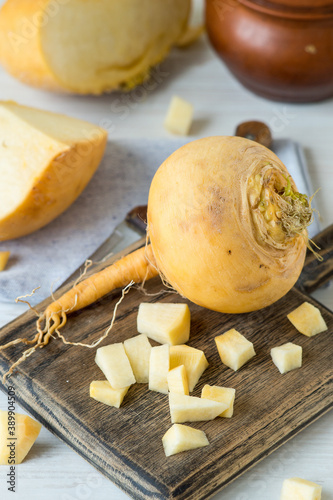 Yellow ripe turnip on a wooden cutting board, next to a small clay pot. Selective focus. Tinted photo.