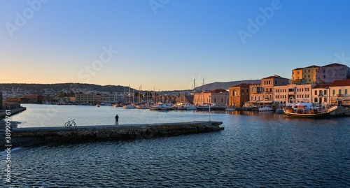 Sunrise at Old Venetian harbour of Chania, Crete, Greece. Unrecognizable male and his bicycle standing on pier and enjoying the view.