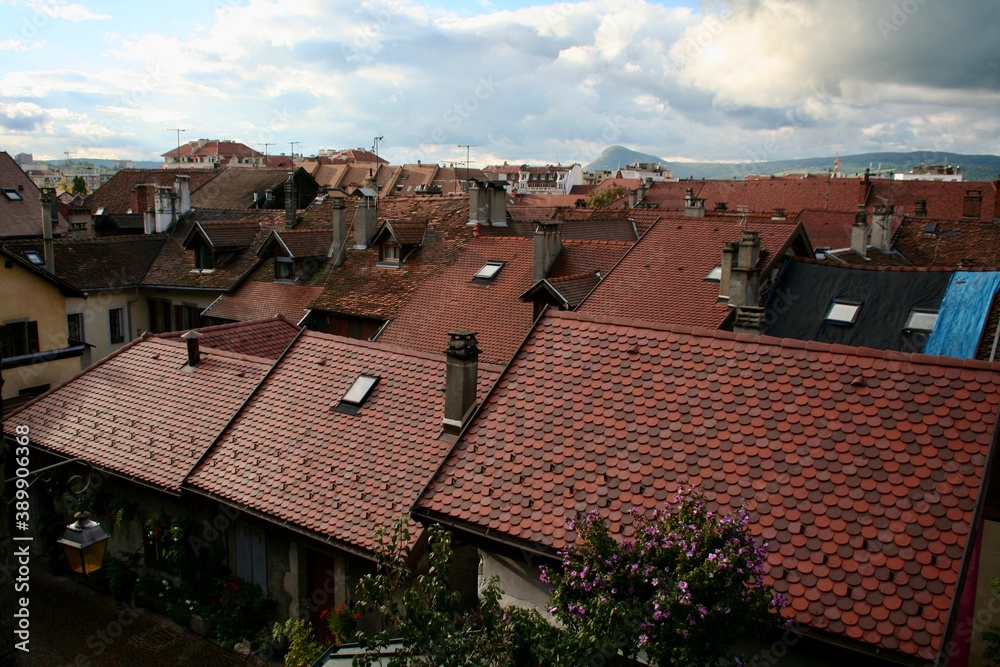Rooftops of an ancient historic city, view covered with red brick colored tiles and chimneys and roof exits and windows. Partly cloudy sky.