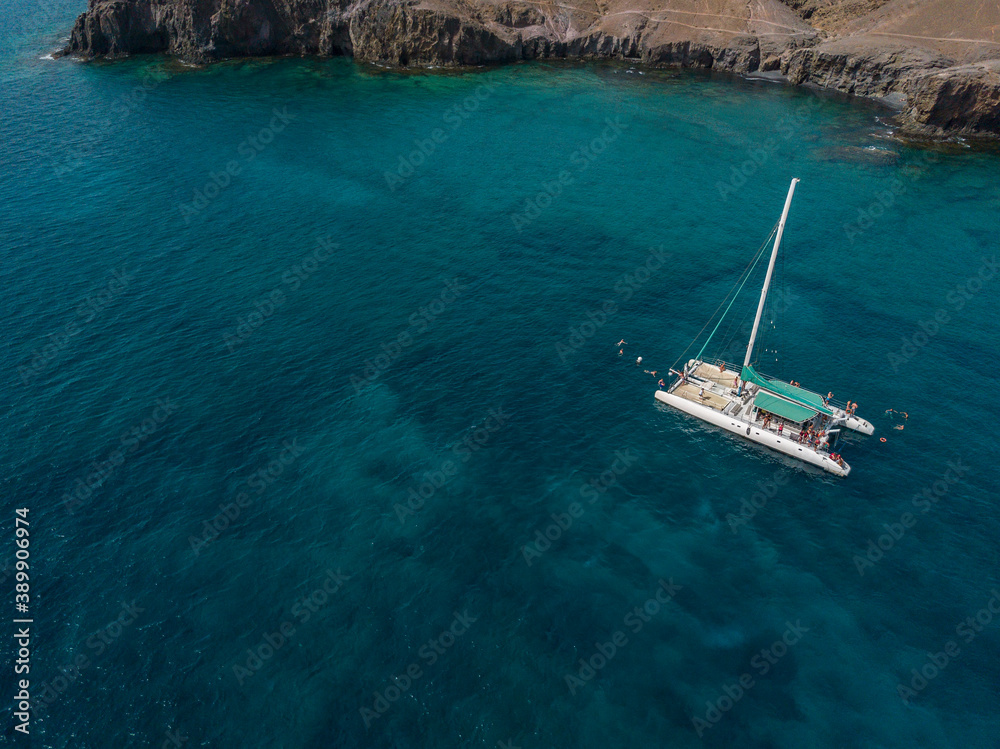 Aerial view of a catamaran with people on board and in the sea, swimming near the coasts of the island of Lanzarote, Canary, Spain. Jet ski performing in the sea
