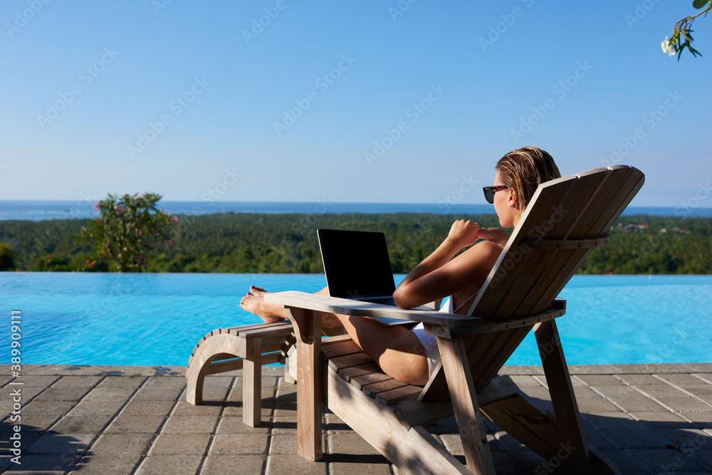 Young female using laptop on sunbed near swimming pool