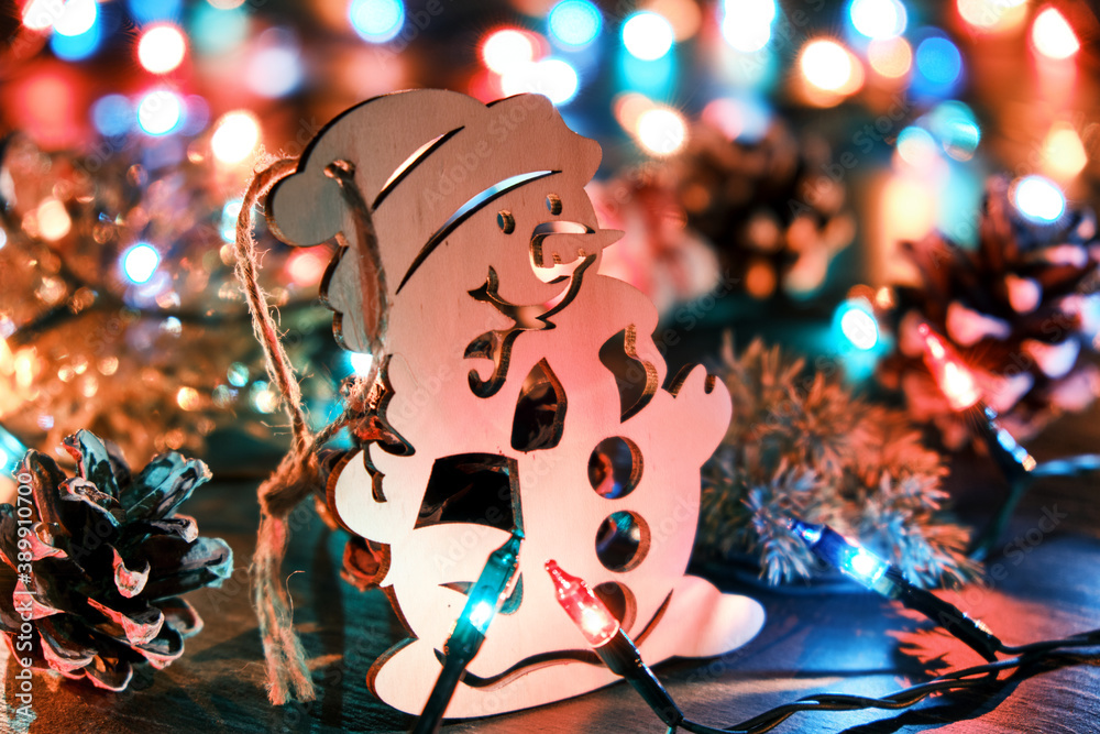 Fototapeta Decorative wooden snowman against the backdrop of blurred christmas lights and other seasonal decorations. Christmas and New Year holiday background