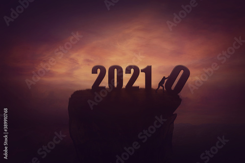 Silhouette of a determined man on the top of a cliff over sunset, announcing the new 2021 year coming, and throws out in the abyss the old 2020. Surreal seasonal scene, change concept and time control