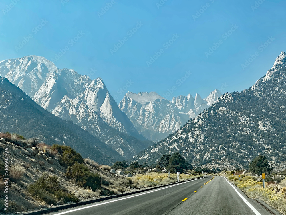Fototapeta premium Long highway extends among hills and snow -capped mountainsL