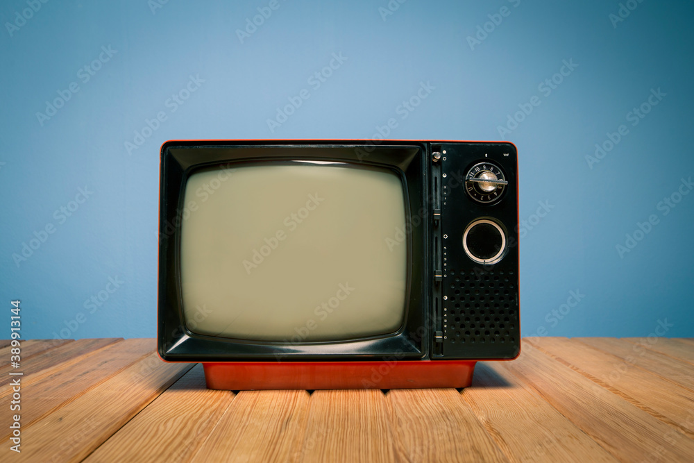 Retro red old television on wood table in front blue concrete wall background. Vintage TV filtered photo