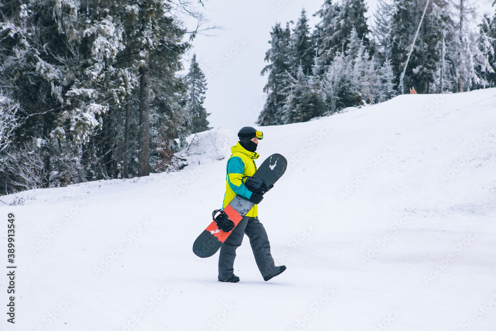 man with snowboard walking by snowed hill man with snowboard walking by snowed hill