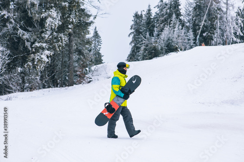 man with snowboard walking by snowed hill