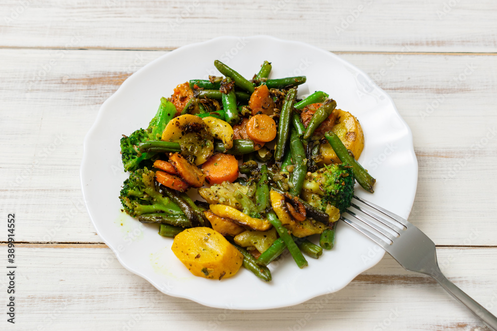 Assorted fried vegetables on a plate on a white wooden background. Mix of carrots, green beans, cauliflower. Assorted fried vegetables on a plate on a white wooden background. Mix of carrots, green beans, cauliflower.