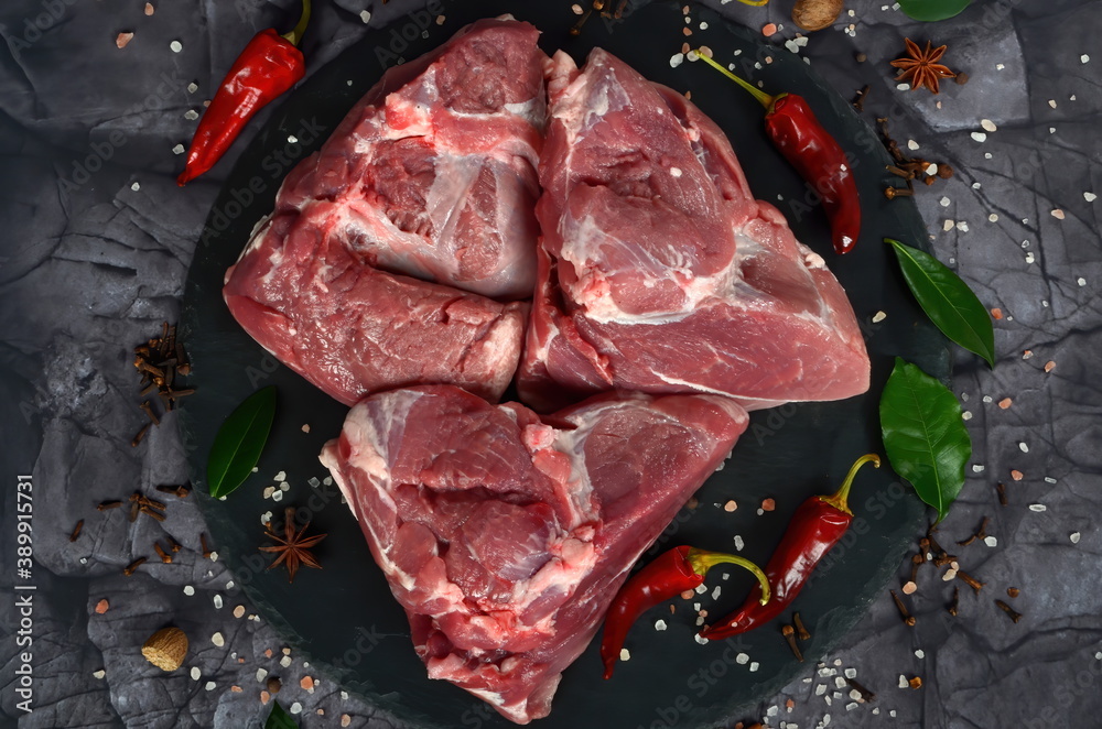 Fresh raw mutton shoulder meat isolated on black stone background with spices. Large piece of shmeat fillet or filet closeup