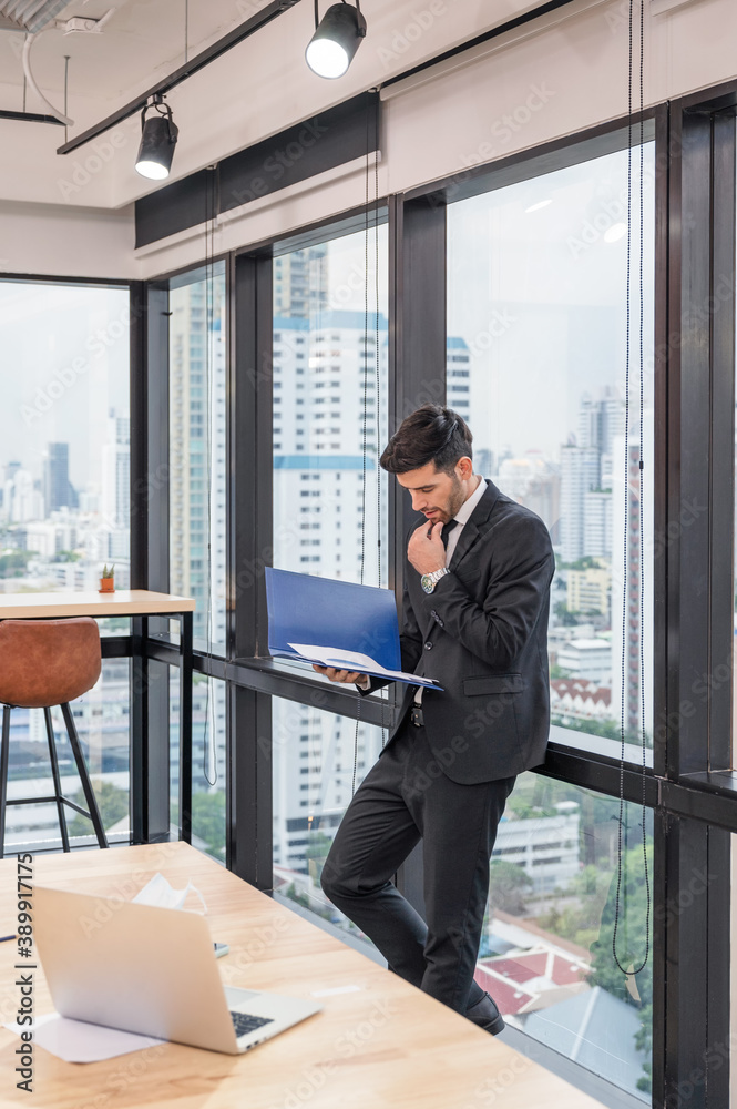 Smart caucasian businessman standing with financial document analysis in modern office Smart caucasian businessman standing with financial document analysis in modern office