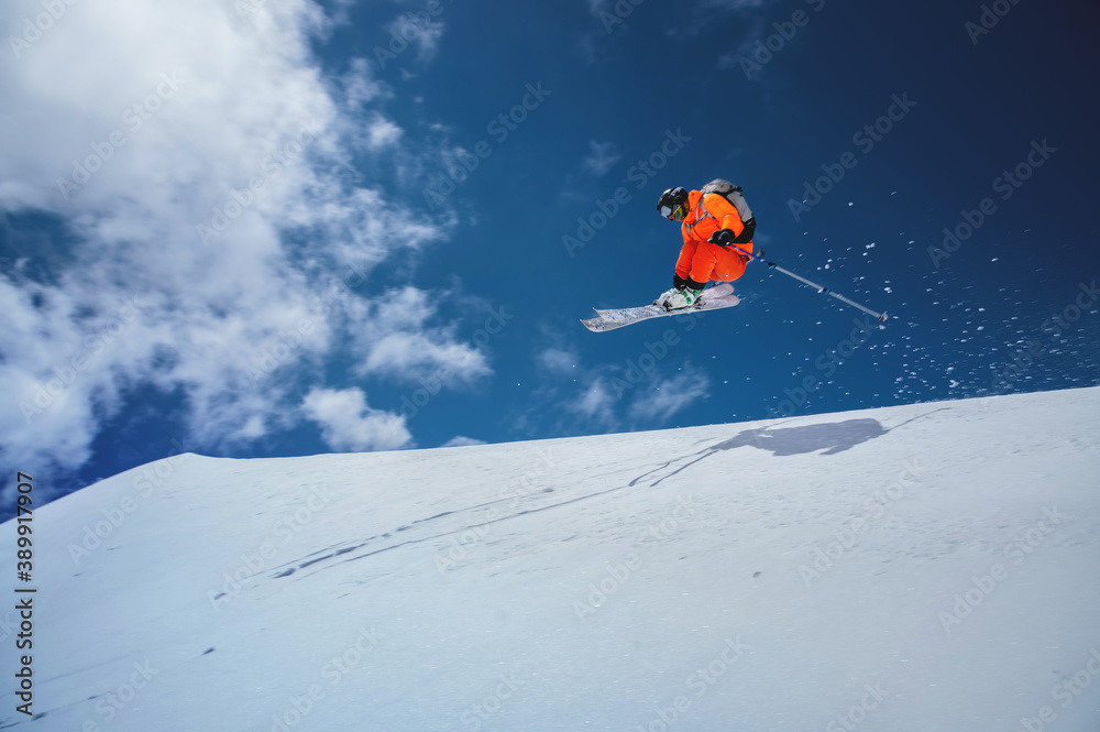 Professional athlete skier freerider in an orange suit with a backpack flies in the air after jumping on the lags on the background of blue sky and snow
