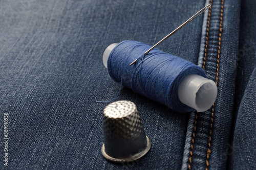 a bobbin of thread with a needle and a thimble. on denim background. close-up.