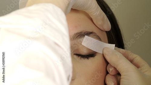 Beautician removes warm wax excess hair from the eyebrow with a special strip. Wax correction of the shape of the eyebrows. Beauty industry close up. Correction of a shape of eyebrows with hot wax