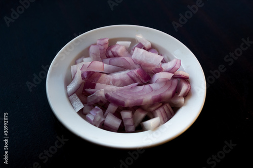 Some diced onions on a plate with a black background.