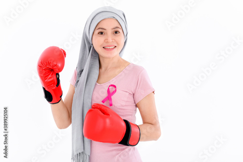 Muslim religious women in hijab put a pink ribbon on their tops. And wearing boxing gloves on a colored background. Breast cancer concept, cancer prevention concept.