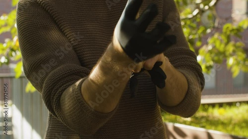 Close up hands of a man putting on black protective latex gloves in the park. Sunny day, early autumn. Protection during viral epidemic.