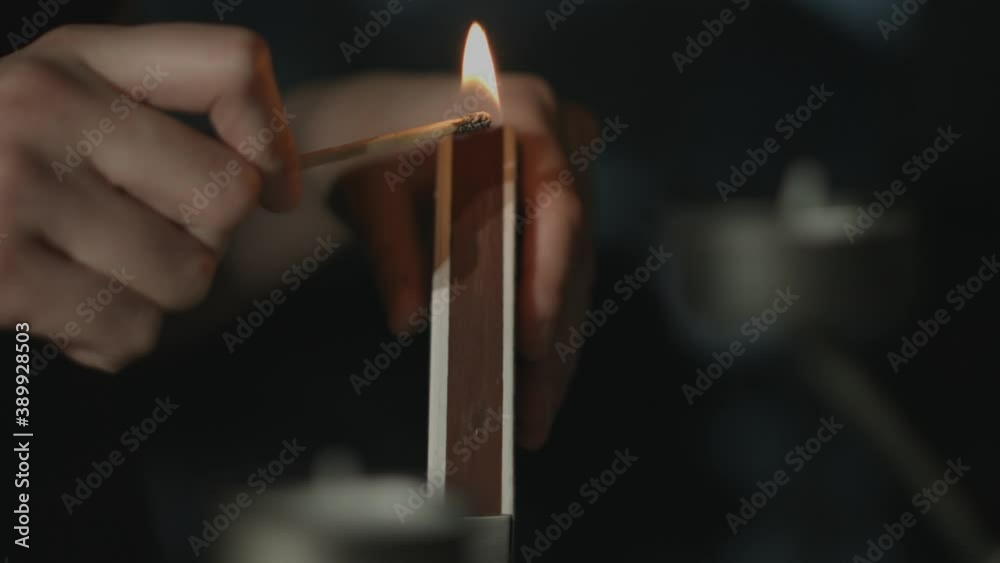 Close up of a match stick being lit and held by a woman with a silver candle holder in the foreground at night. Shot in 4K.