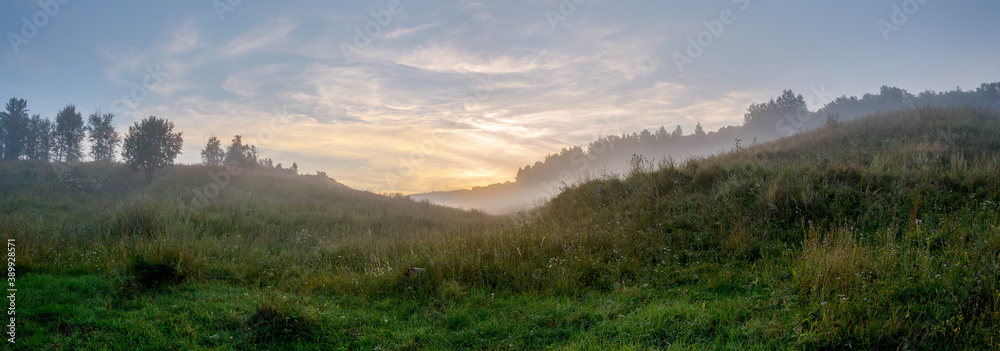 Beautiful summer hazy landscape with foggy hollow and green hills before the sunrise