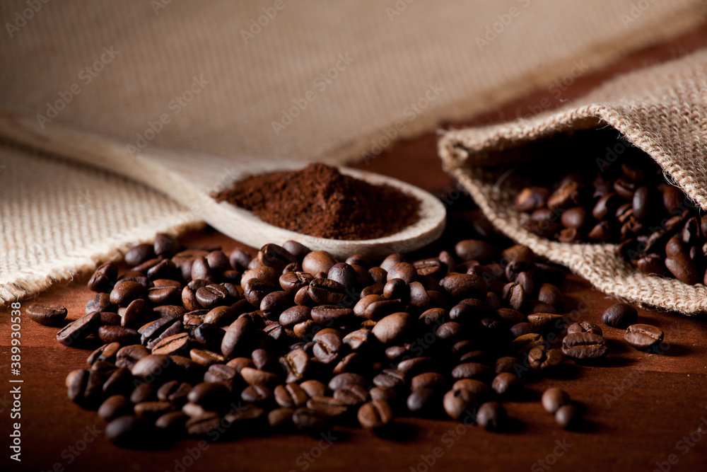 Fototapeta premium coffee beans, and wooden spoon with ground coffee, raffia cloth bag, brown background