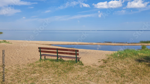 A bench on the shore of the lake. The calm water merges with the sky.