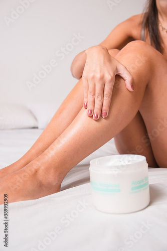 woman sitting on bed putting moisturizer on her legs in her grooming routine