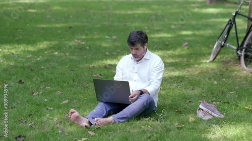An adult businessman wearing an American jacket works outdoors in a park with buildings