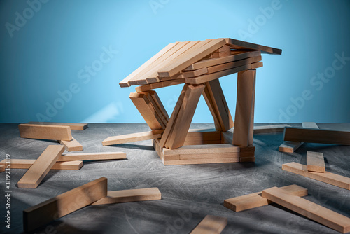 Collapsing house made of wooden blocks on a blue background and randomly lying blocks.