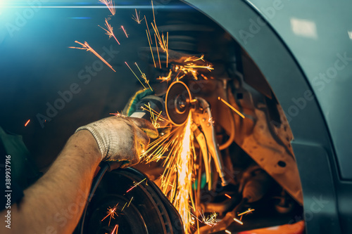 Car repair, worker sawing rusted bolt with circular saw, sparks fly, auto repair shop. photo