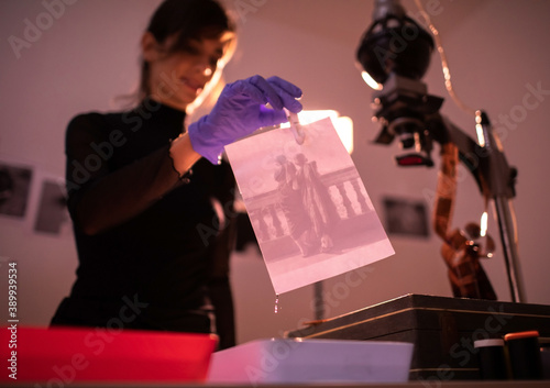 Female photographer developing film and printing photographs in traditional process in darkroom. Portrait of creative girl photographer in photo studio darkroom. Developing analog camera film. photo