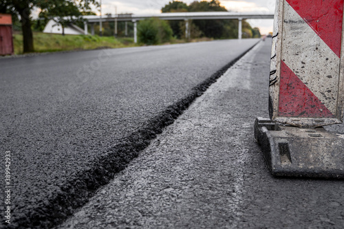 A large layer of fresh hot asphalt. Layer of asphalt raw material in a shallow depth of field. Rollers rollin fresh hot asphalt on the new road. Road construction. Construction of a new road.