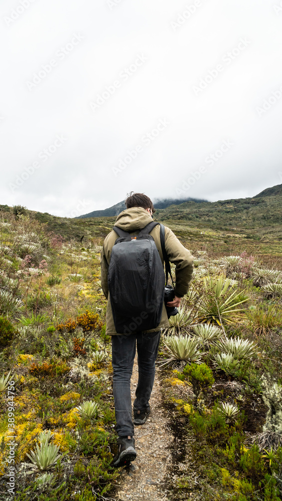 A man walking with a camera in a green mountain.