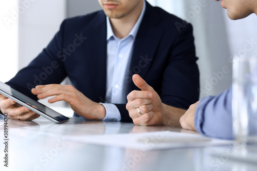Business people using tablet computer while working together at the desk in modern office. Unknown businessman or male entrepreneur with colleague at workplace. Teamwork and partnership concept