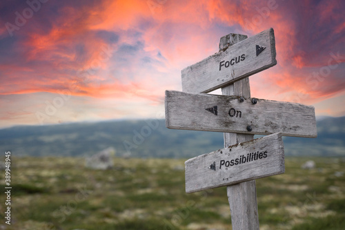 focus on possibilities text engraved in wooden signpost outdoors in nature during sunset and pink skies. photo