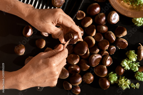Preparing chestnuts for frying. Top view of chestnuts and woman's hands prepares chestnuts. A seasonal dish for christmas or holidays
