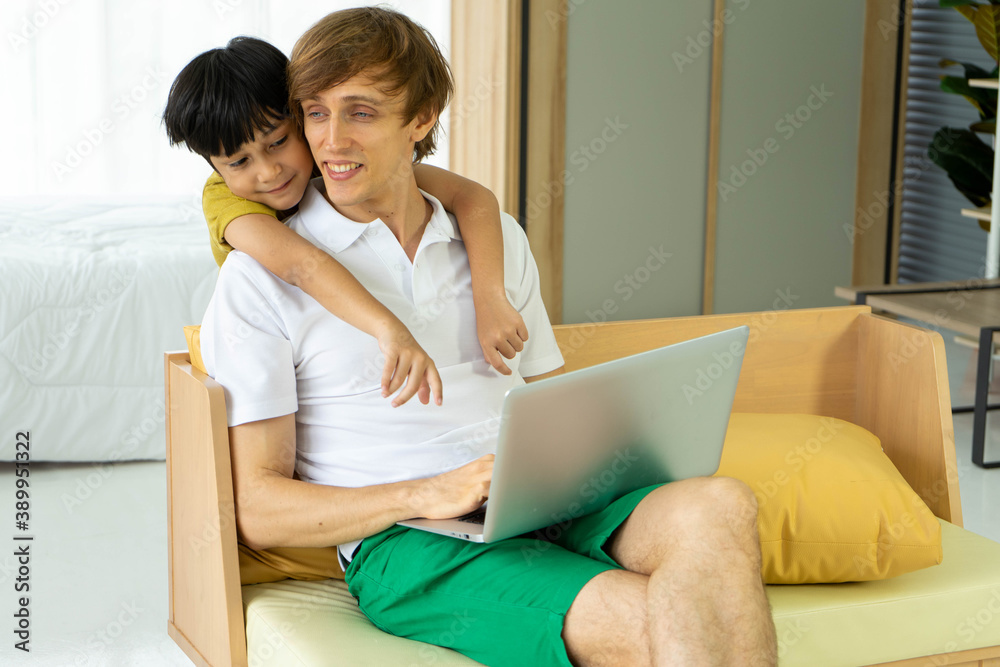 Young caucasian businessman and father working from home with notebook computer and taking care of little son in living room. Social distancing new normal concept. Young caucasian businessman and father working from home with notebook computer and taking care of little son in living room. Social distancing new normal concept.
