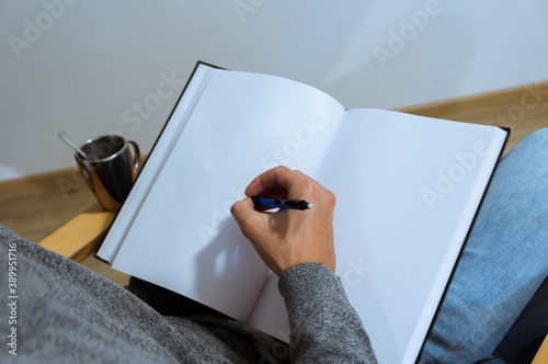 young male student taking notes. Hand drawing on a blank book on an armchair. over the shoulder view.