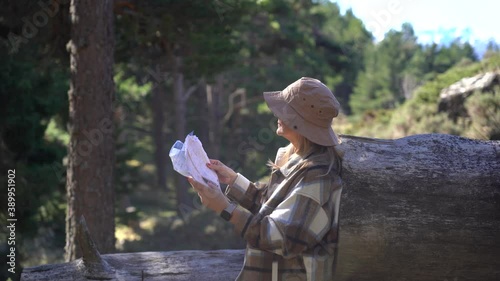 A woman with a hat looks at a map in a forest