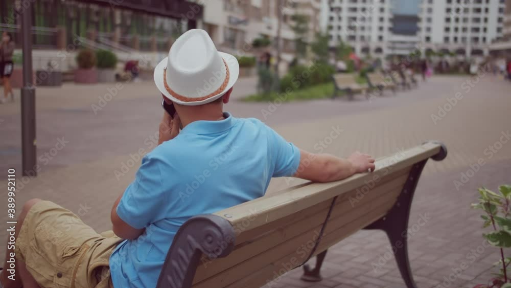 A man tourist in a white hat is resting while sitting on a city bench, camera movement, copy space