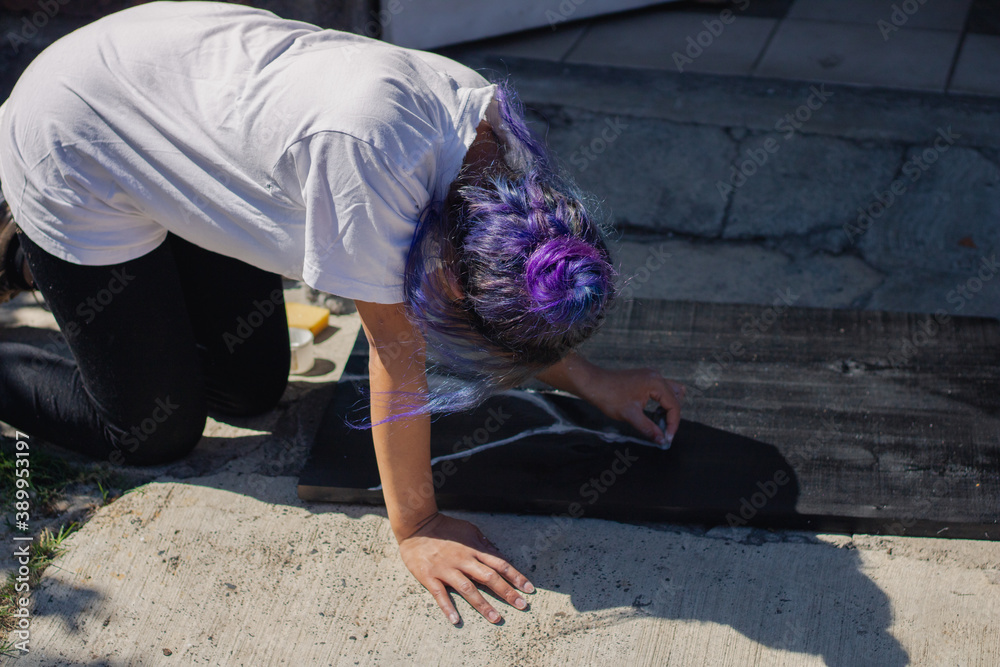 Latin hispanic woman with colorful hair painting a wooden board with black and white paint. Outdoors painting hobbie