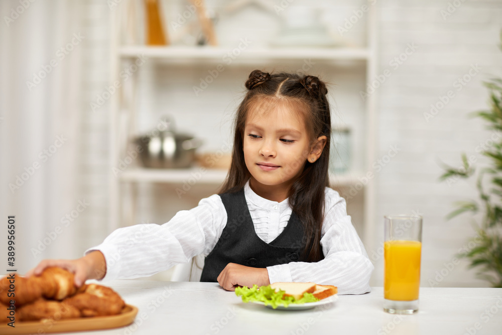 happy little child girl in school uniform having breakfast - sandwich and orange juice in the kitchen. healthy breakfast happy little child girl in school uniform having breakfast - sandwich and orange juice in the kitchen. healthy breakfast