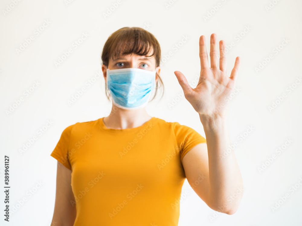 Young woman in yellow T-shirt wearing face mask with serious look making stop sign with hand Young woman in yellow T-shirt wearing face mask with serious look making stop sign with hand