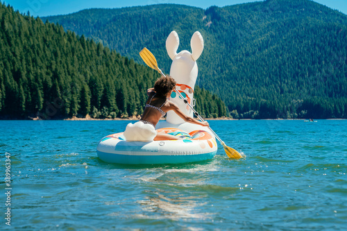 Foto Teen girl paddling on lake in inflatable llama pool floaty