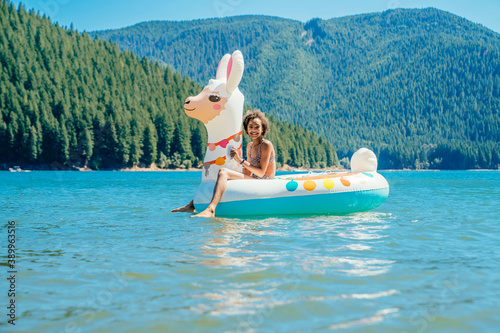 Smiling teen girl sitting on inflatable llama pool floaty in lake in forest in summer