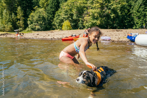 Fototapeta Naklejka Na Ścianę i Meble -  Happy girl swimming in lake with pet dog in life jacket